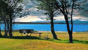 Un banco junto a un lago, con árboles y montañas al fondo.