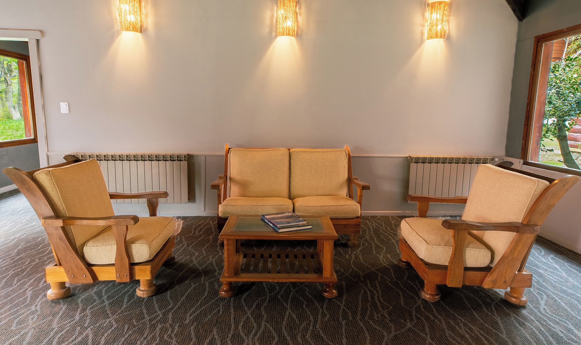Una habitación con sofá, dos sillones, una mesa de centro y tres luces fijadas a la pared.