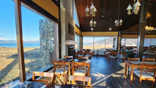 A restaurant with wooden tables and chairs, large windows, and hanging chandeliers. - Tolkeyen (Ushuaia)