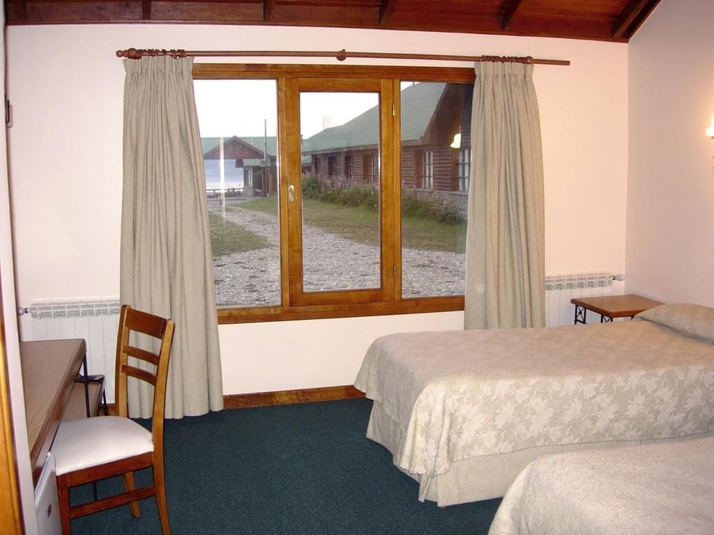 Una habitación con una cama, una silla, una mesa y una ventana con cortinas.
