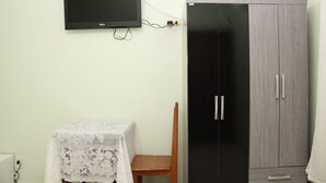 Ein Zimmer mit einem schwarzen Kleiderschrank, einem Tisch mit weißer Spitze und einem an der Wand befestigten Fernseher.