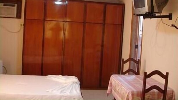 Ein Zimmer mit einem Bett, einem kleinen Tisch, einem Fernseher auf einem Schrank und einem Kleiderschrank.