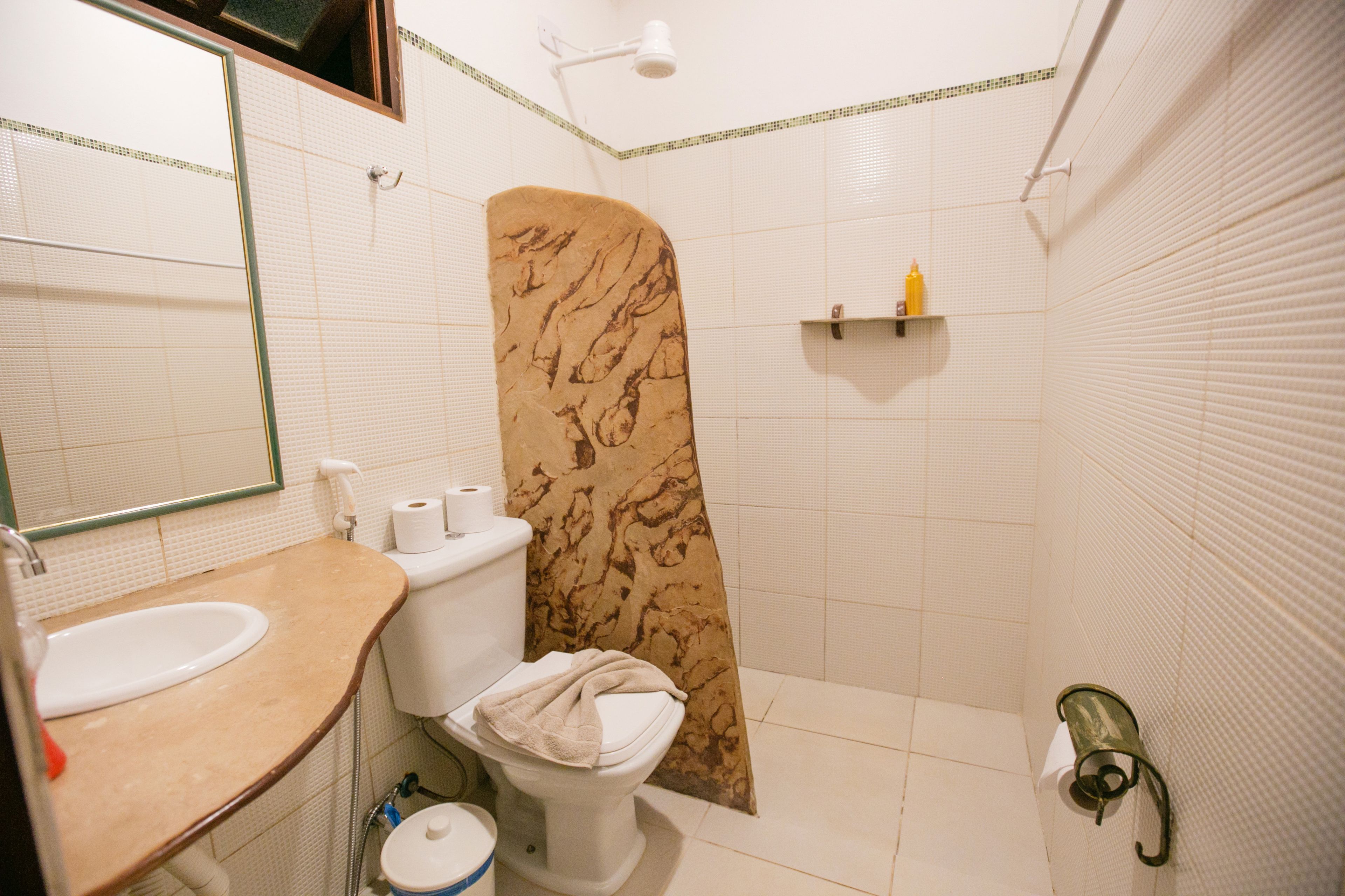 A bathroom with a sink, toilet, shower curtain, and a shelf with toiletries.