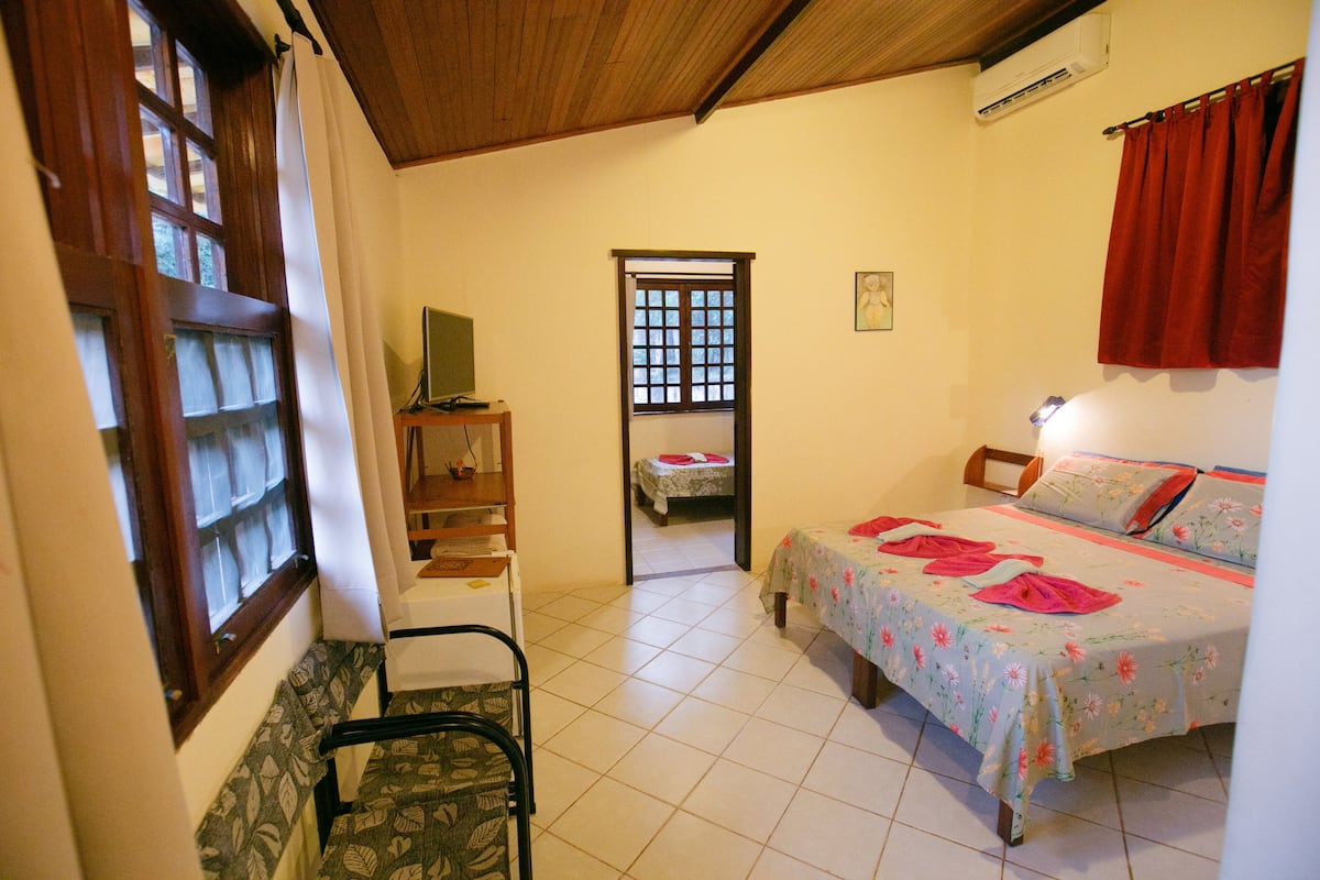 Quarto com uma cama, uma cadeira, uma escrivaninha e uma janela.