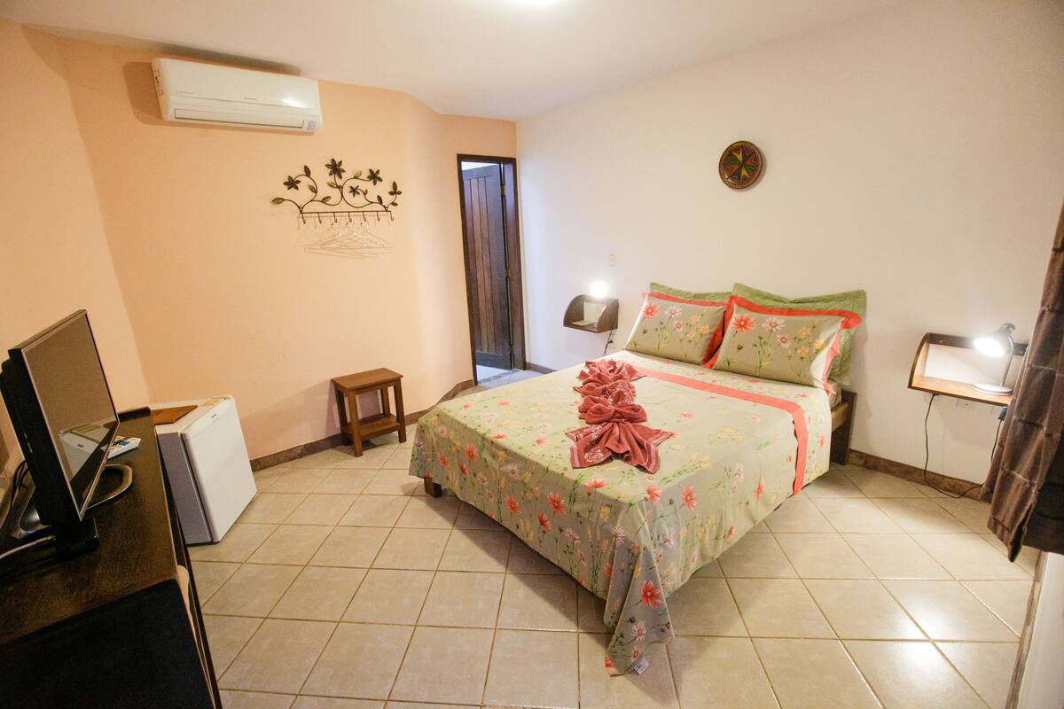 Quarto com cama, escrivaninha, cadeira, mesa pequena, ar condicionado e porta.