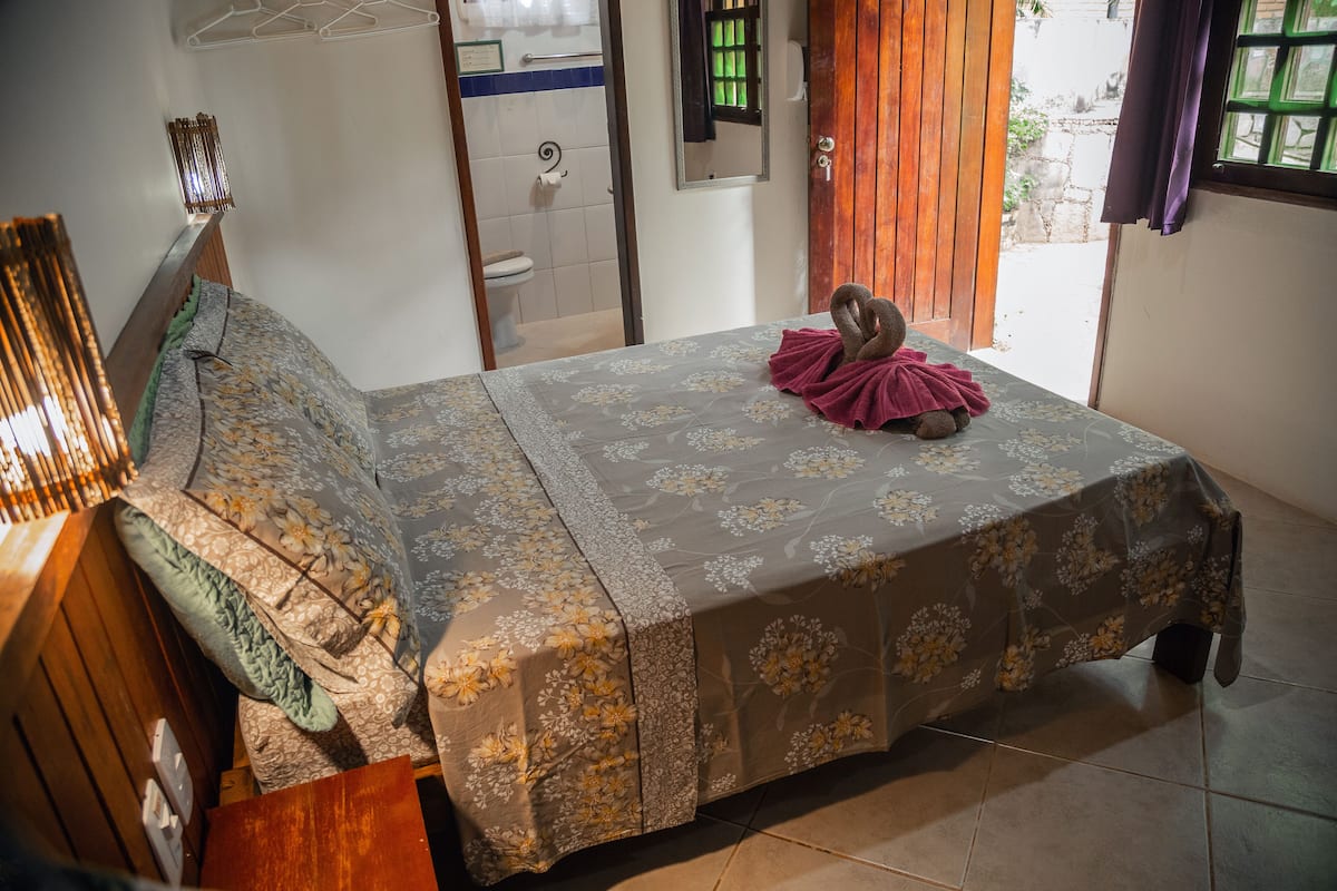 Cama bem arrumada com roupa de cama floral, cabeceira de madeira e um pequeno objeto decorativo sobre a cama.