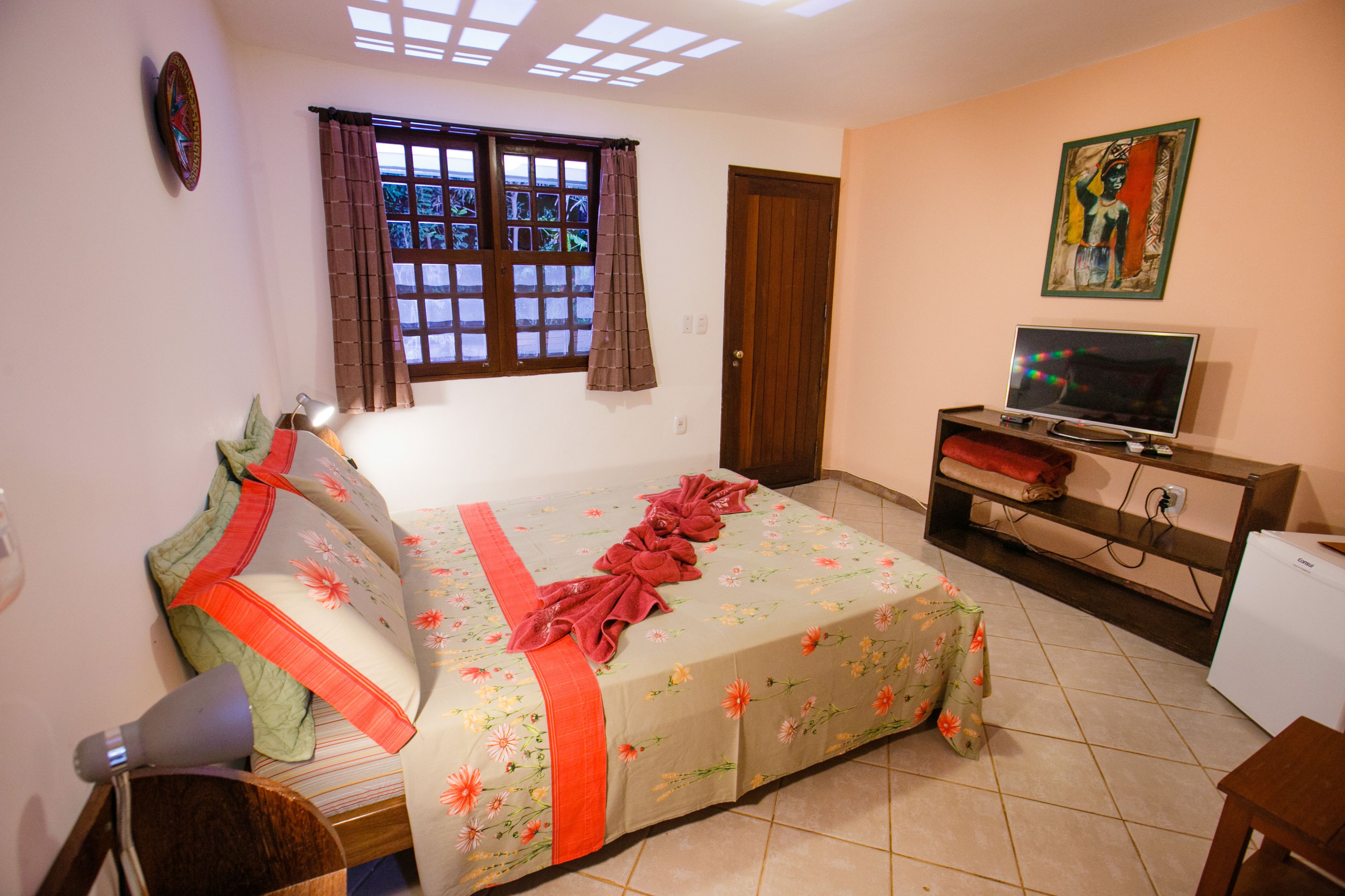 Un dormitorio con cama, televisor, escritorio y ventana con cortinas.