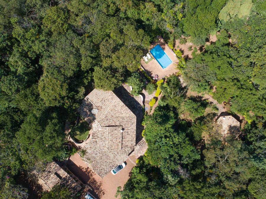 Vista aérea de una propiedad con un edificio central rodeado de bosque denso. Hay una piscina con zona de sol y un pequeño jardín.