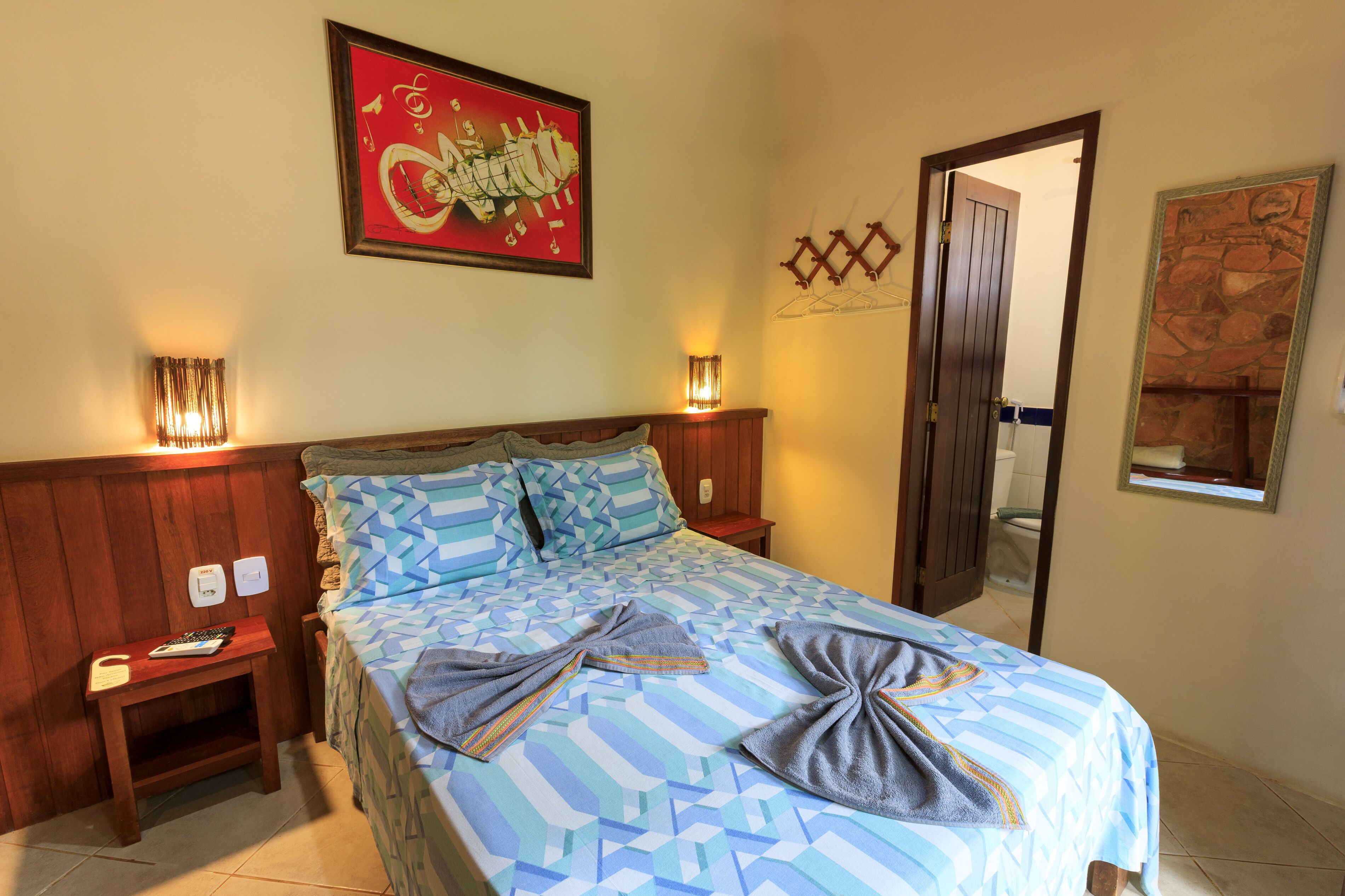 A hotel room with a bed, bedside tables, a wall-mounted artwork, and a door leading to a bathroom.