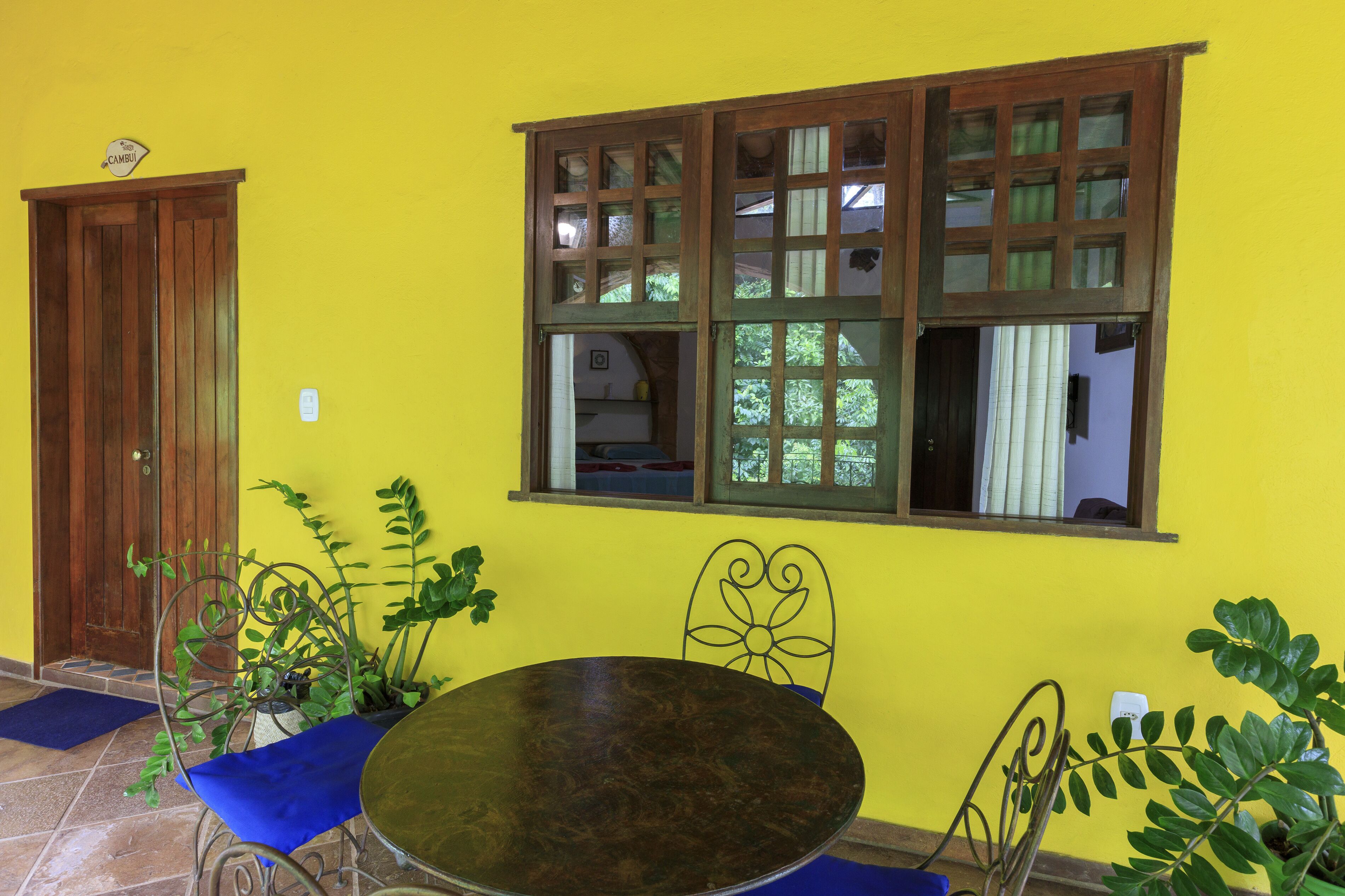 Una habitación con una pared amarilla, una puerta de madera, un ventanal con múltiples divisiones, una mesa redonda y dos sillas.