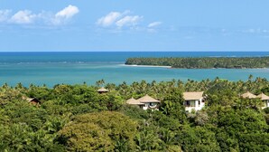 Een tropisch resort met meerdere bungalowachtige gebouwen, omringd door dicht bos, met uitzicht op een heldere blauwe zee en een zandstrand.