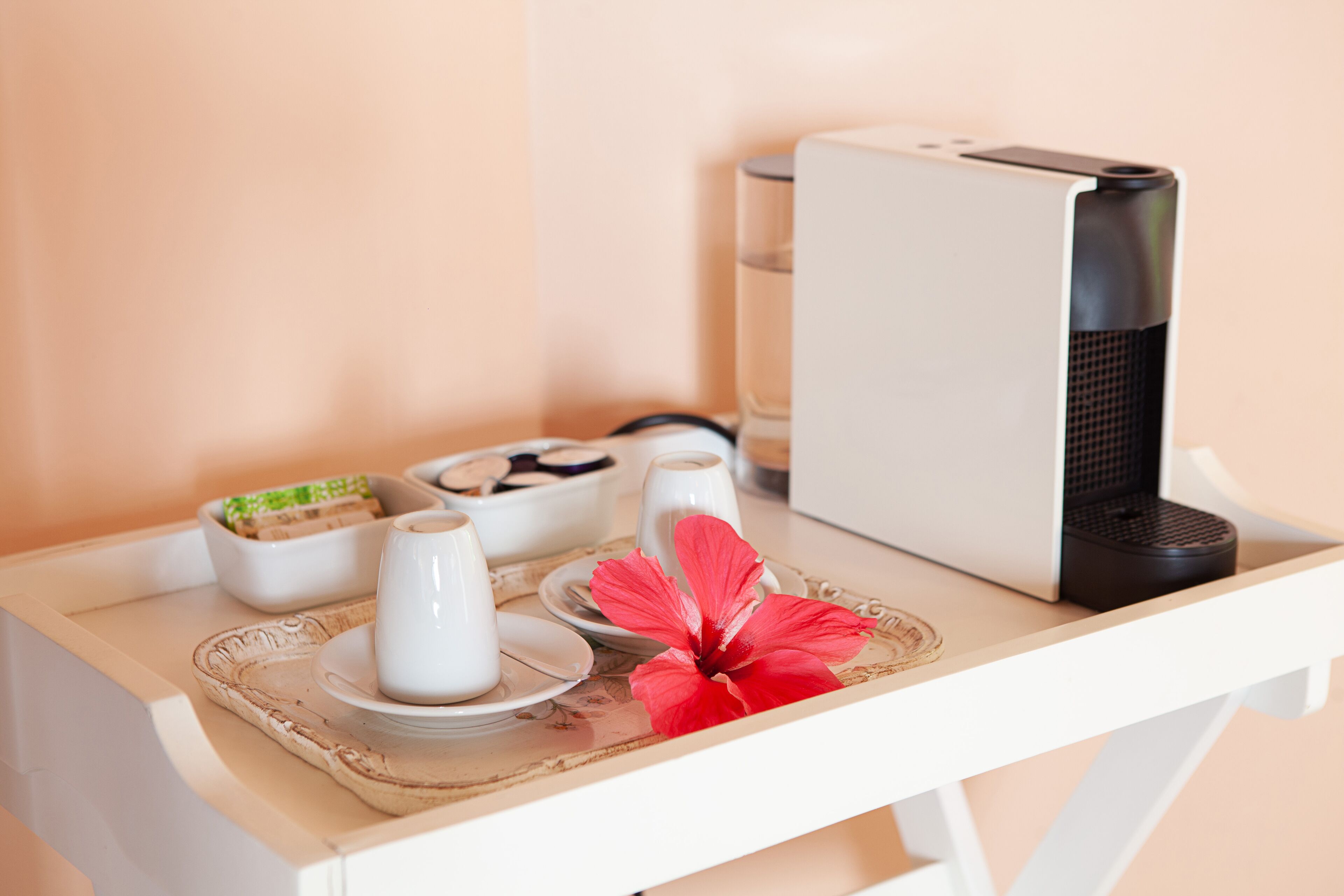 A table with a coffee maker, cups, plates, and a decorative flower.