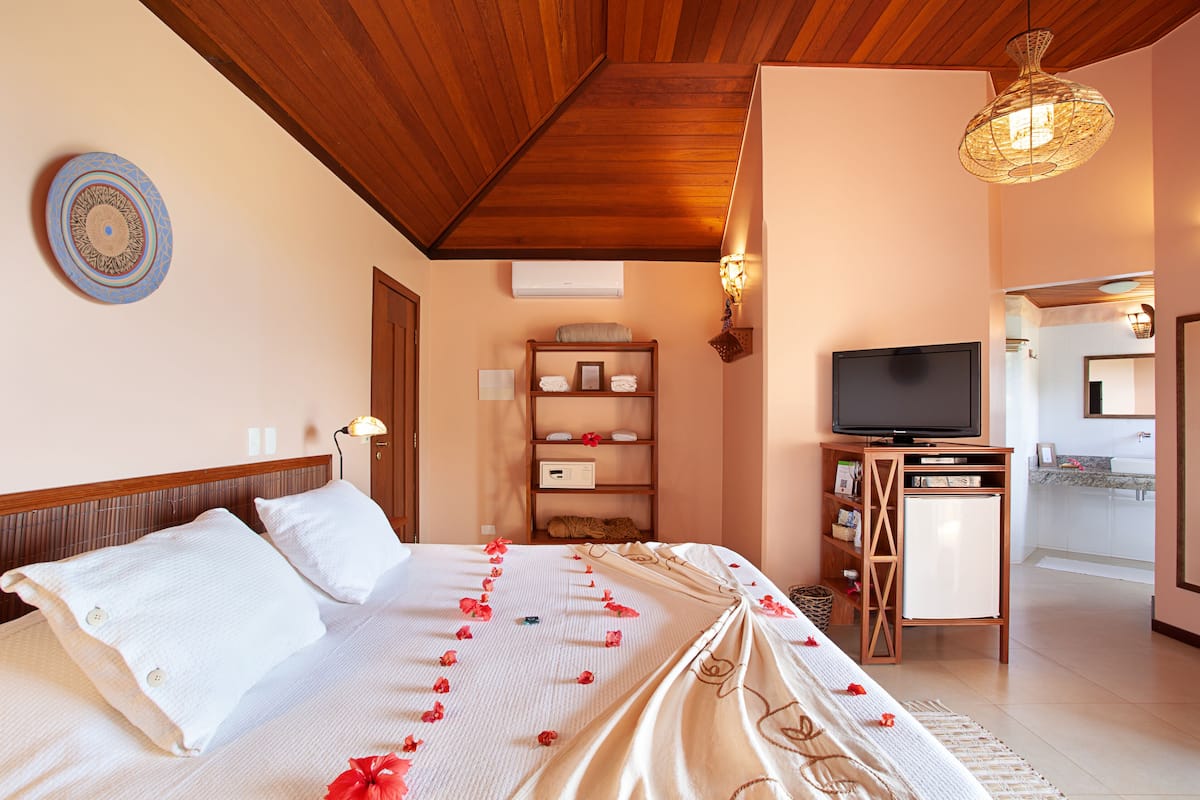 Une chambre d’hôtel avec un plafond en bois, un lit avec du linge de maison blanc, une télévision et une petite kitchenette.