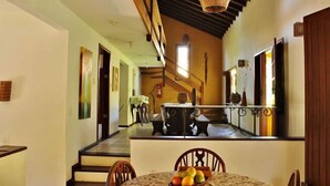 A dining area with a table set for two, a staircase leading to an upper level, and a view of a kitchen area. - Casa Grande & Senzala (Porto Seguro)