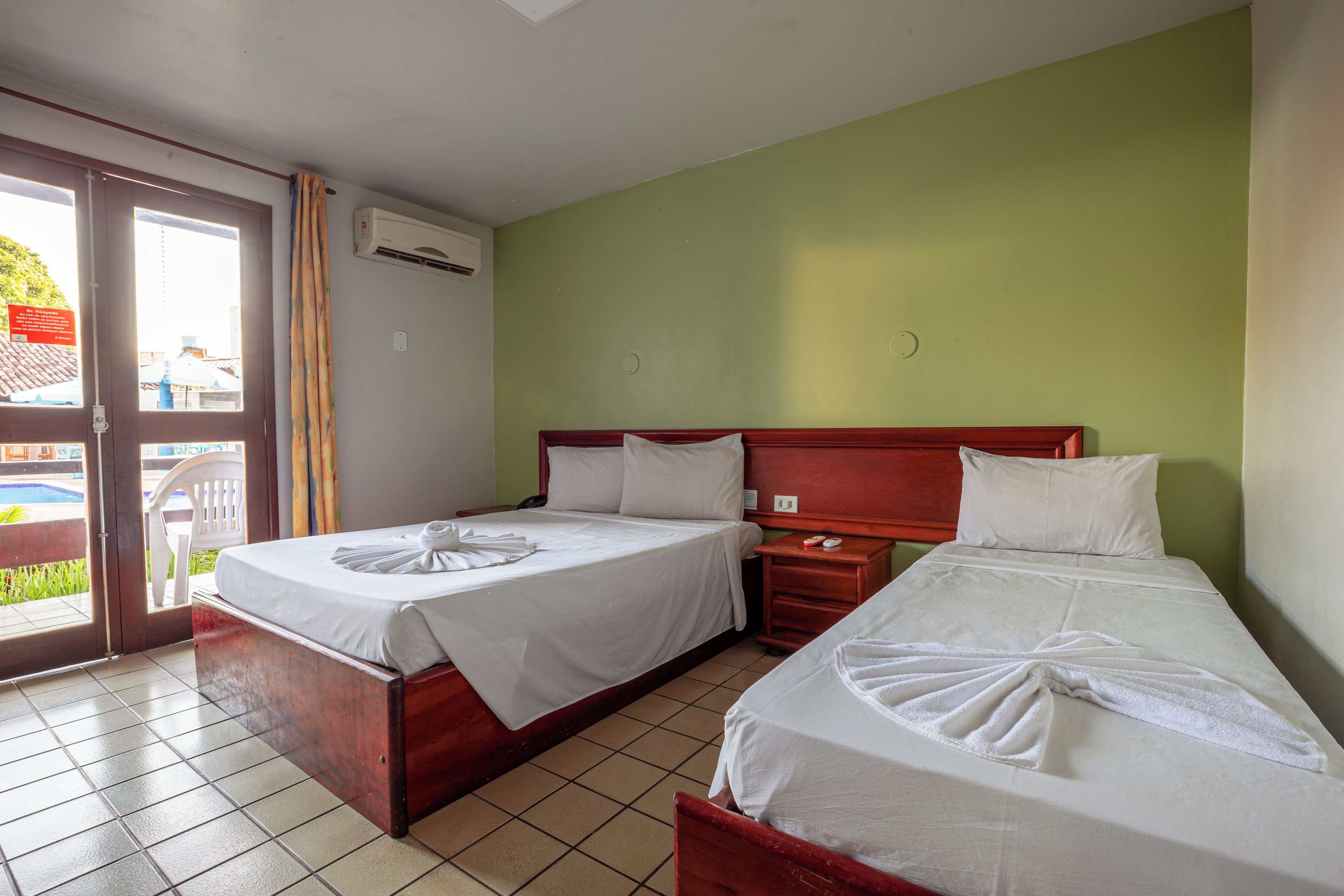A hotel room with two beds, a wooden headboard, a small bedside table, and a window with curtains.
