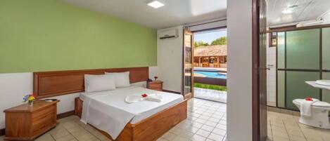 A hotel room with a wooden bed, a nightstand, a bathroom with a sink and toilet, and a view of an outdoor pool area.