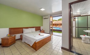 Une chambre d’hôtel avec un lit en bois, une table de chevet, une salle de bain avec un lavabo et des toilettes, et une vue sur l’espace extérieur abritant une piscine.
