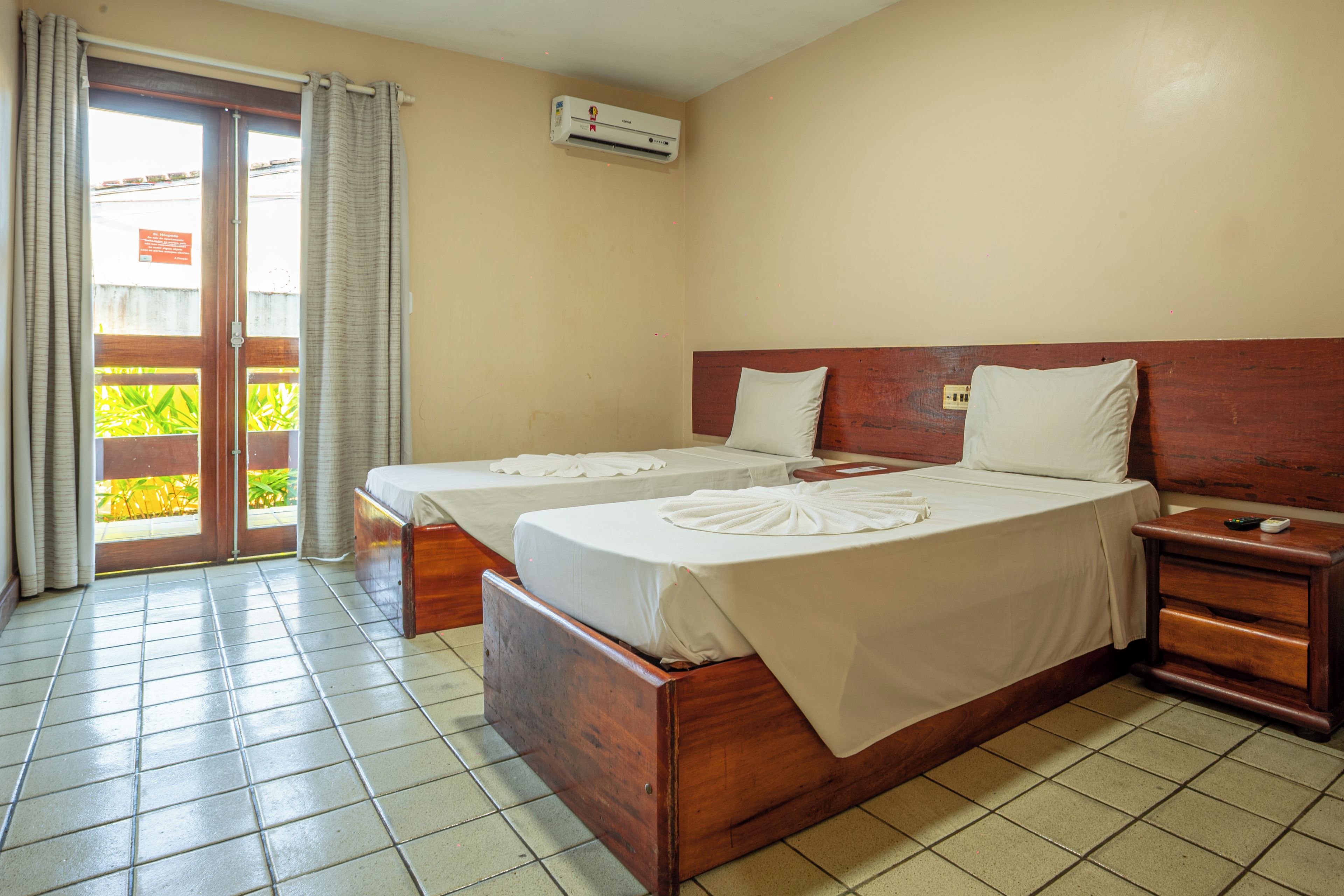 A hotel room with two beds, a wooden headboard, a nightstand, and a sliding glass door leading to a balcony.
