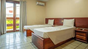 A hotel room with two beds, a wooden headboard, a nightstand, and a sliding glass door leading to a balcony.