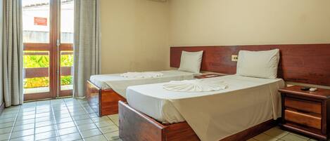 A hotel room with two beds, a wooden headboard, a nightstand, and a sliding glass door leading to a balcony.