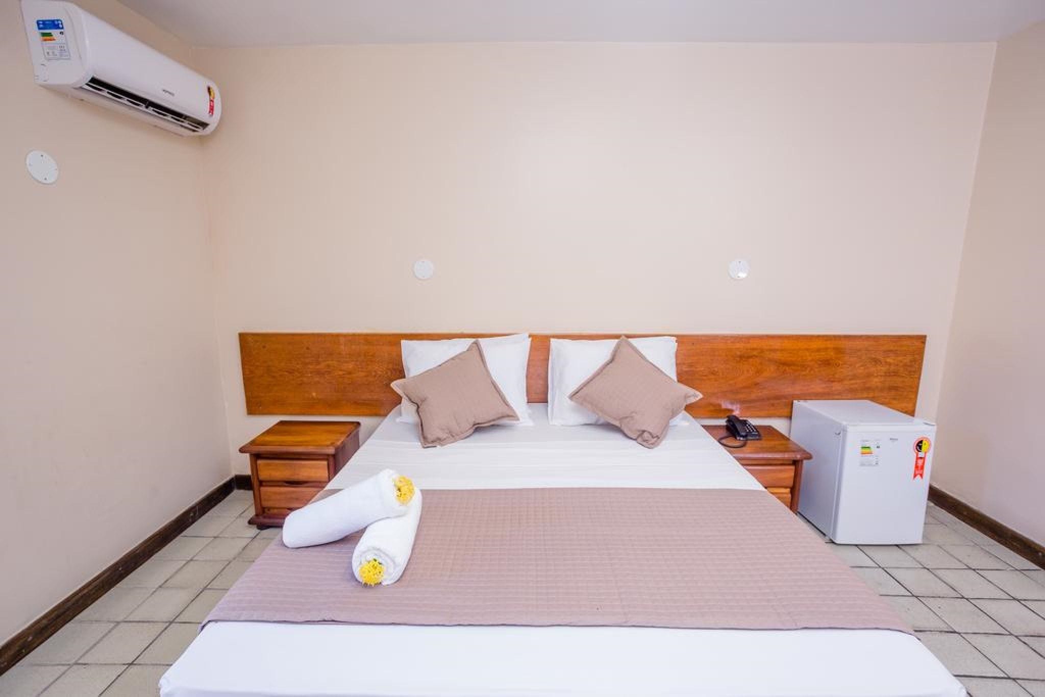 Een hotelkamer met een bed, twee nachtkastjes, een kleine koelkast en een airconditioning.
