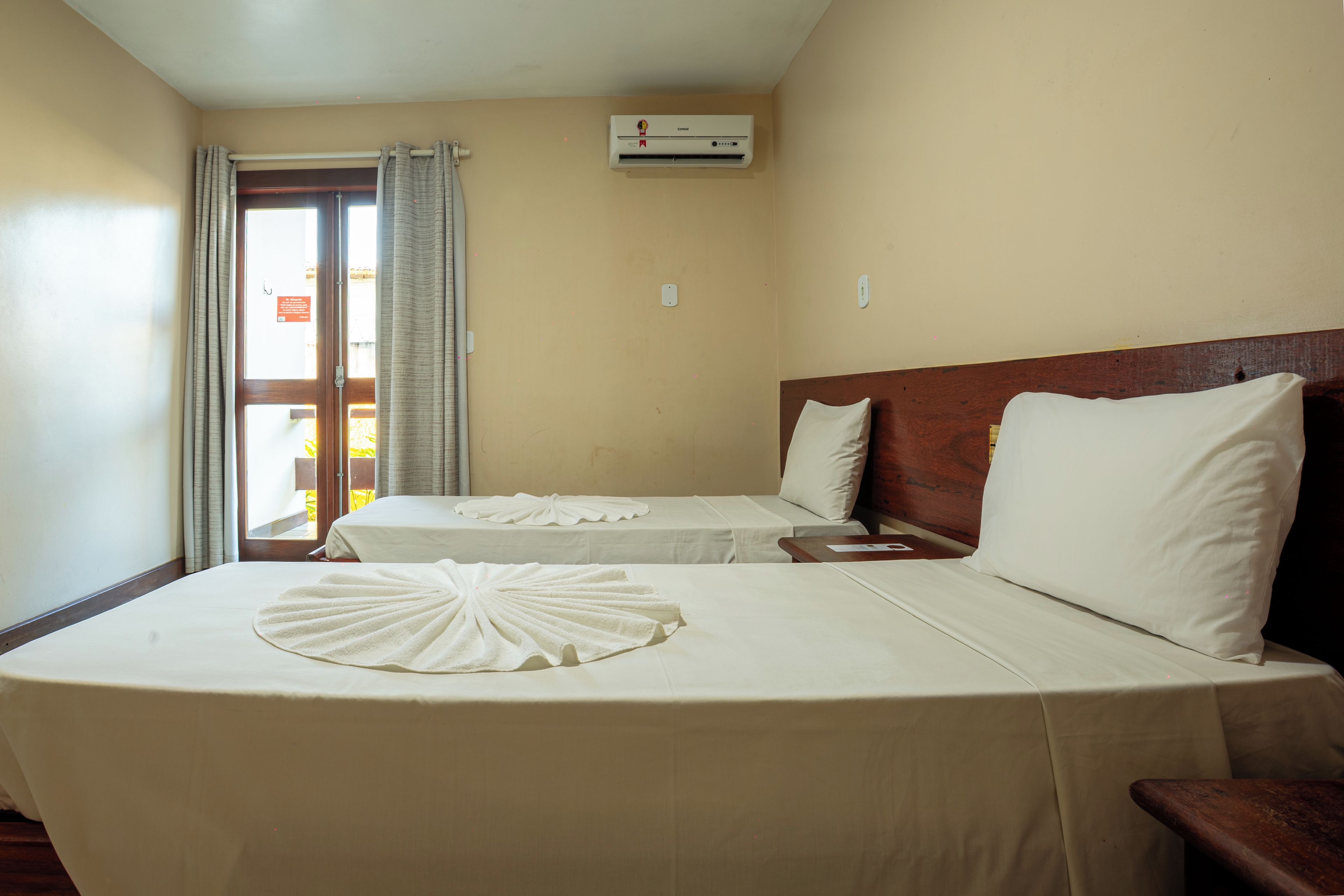 Une chambre d’hôtel avec deux lits, une tête de lit en bois, une fenêtre avec des rideaux et un appareil de climatisation.