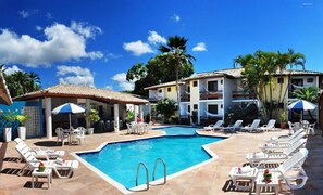 A pool area with lounge chairs and umbrellas, a building with balconies, and palm trees. - Rede Andrade Estrela Dalva Centro (Porto Seguro)