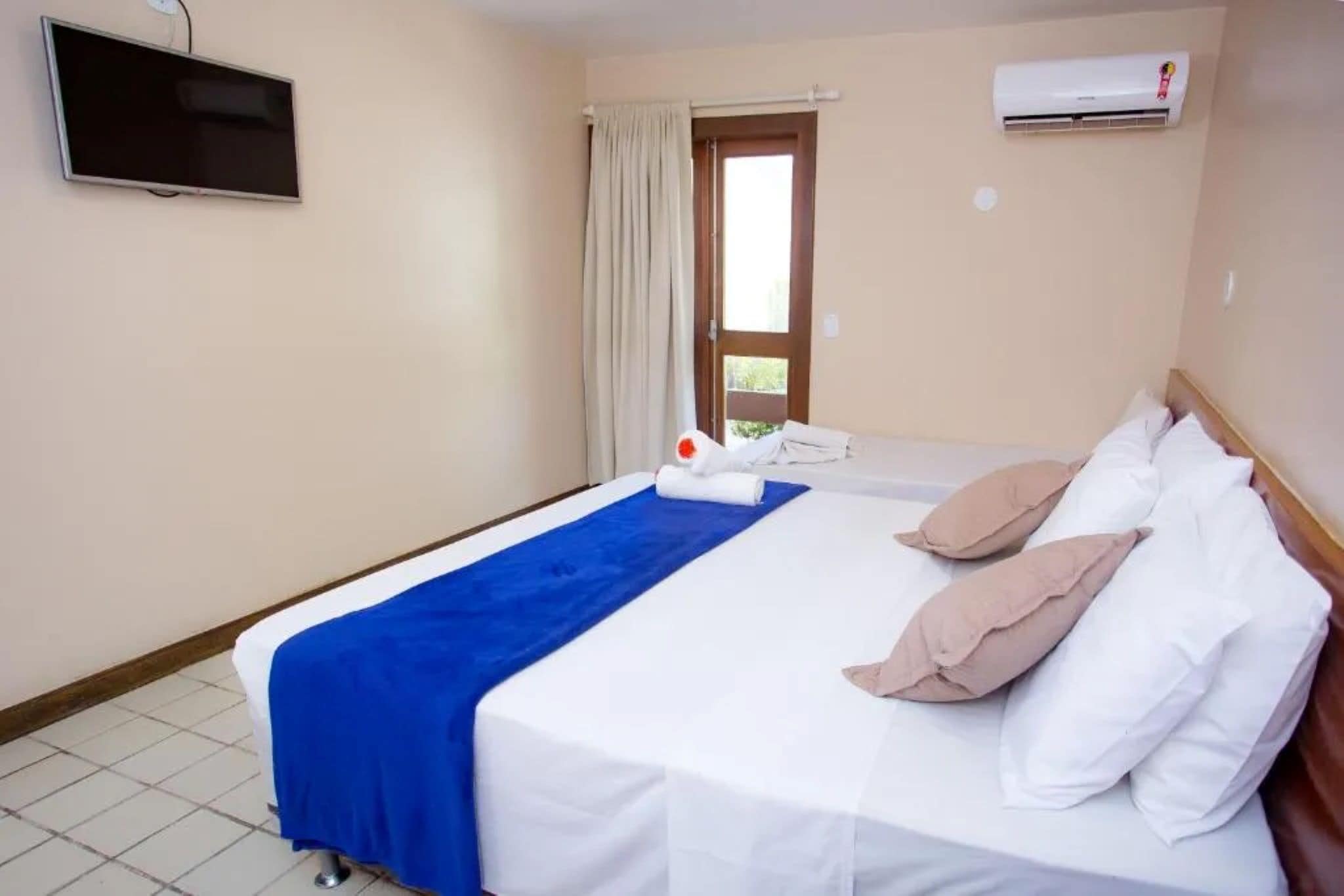 Una camera d'albergo con un letto, una televisione, un condizionatore d'aria e una finestra con tende.