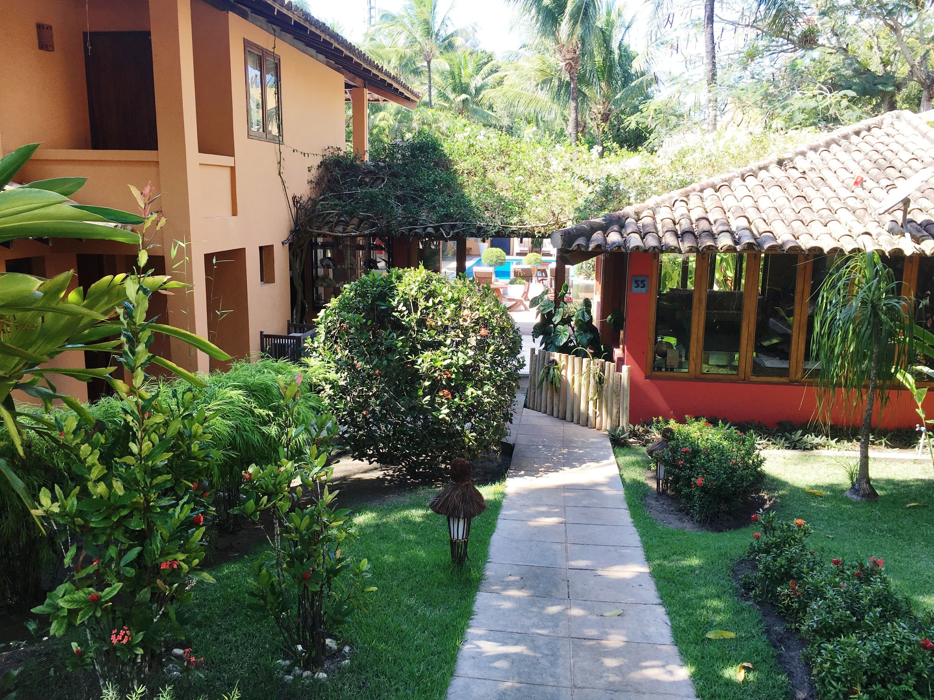 A pathway leading to a building with a tiled roof, surrounded by lush greenery and a well-maintained garden.