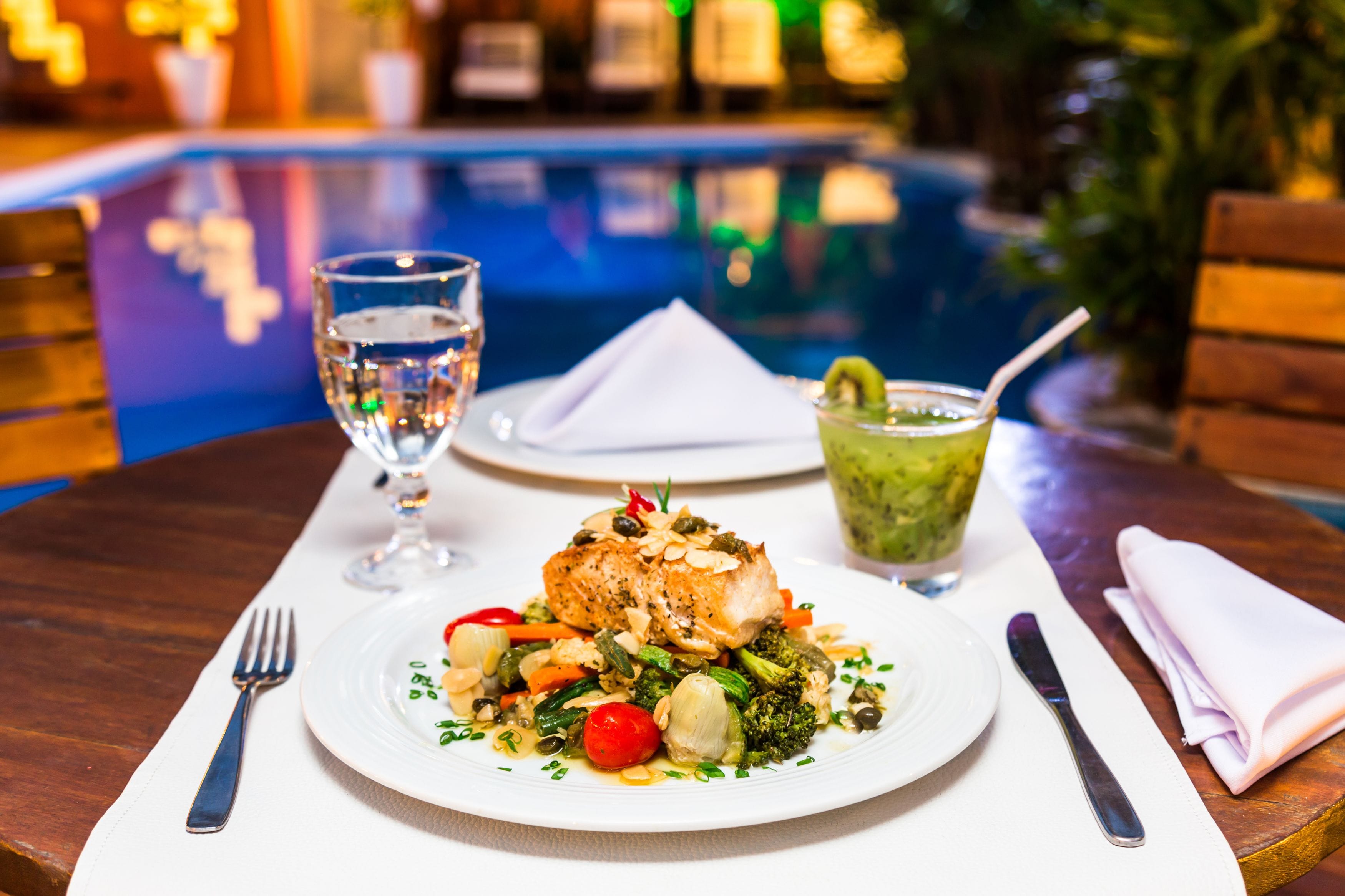 A dining table with a plate of food, a glass of water, and a cocktail.