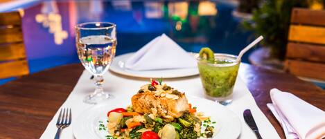 A dining table with a plate of food, a glass of water, and a cocktail.