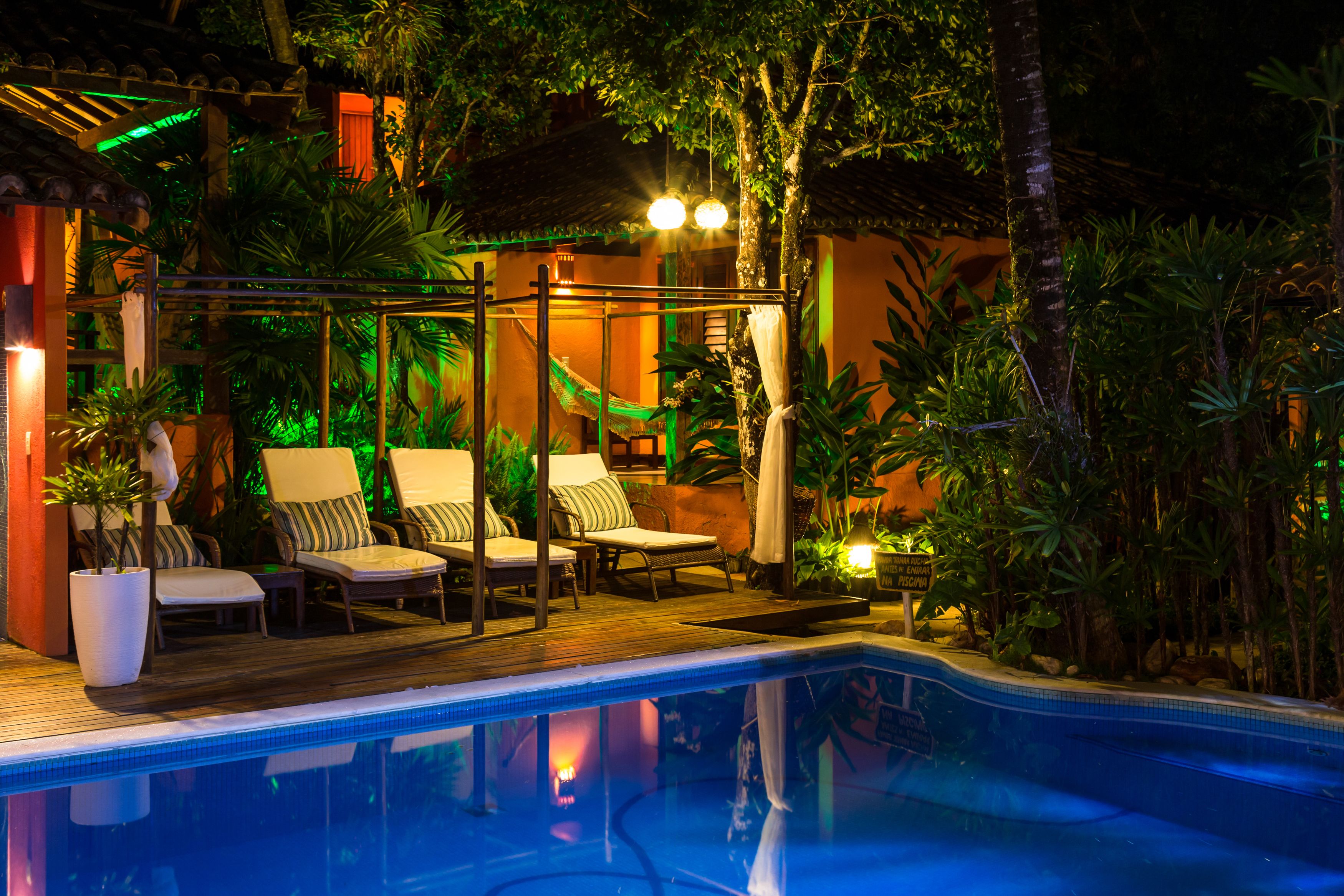 A pool area with lounge chairs and a hammock, surrounded by tropical plants and a wooden deck.