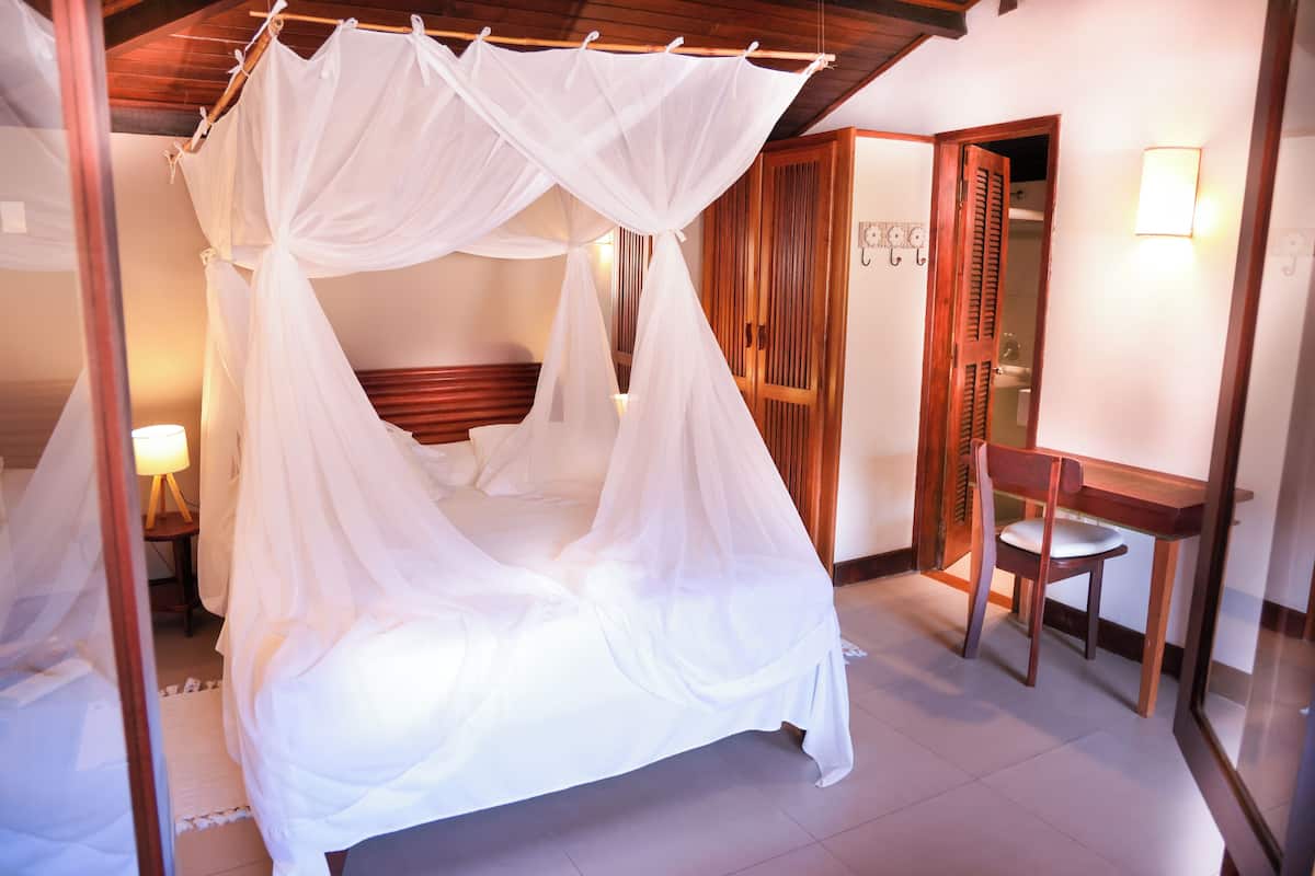A four-poster bed with a canopy, a wooden chair, a bedside table, and a nightstand with a lamp.