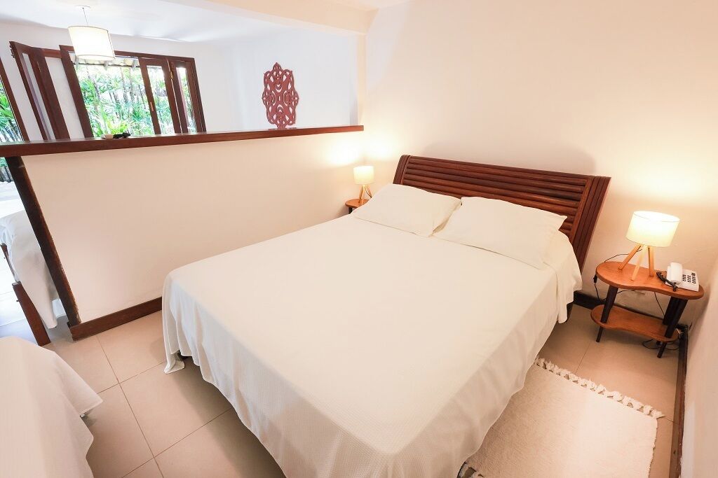 A neatly made bed with white linens, two bedside tables with lamps, and a wooden headboard.