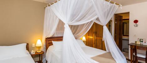 A hotel room with a bed under a canopy, a bedside table with a lamp, and a desk with a chair.