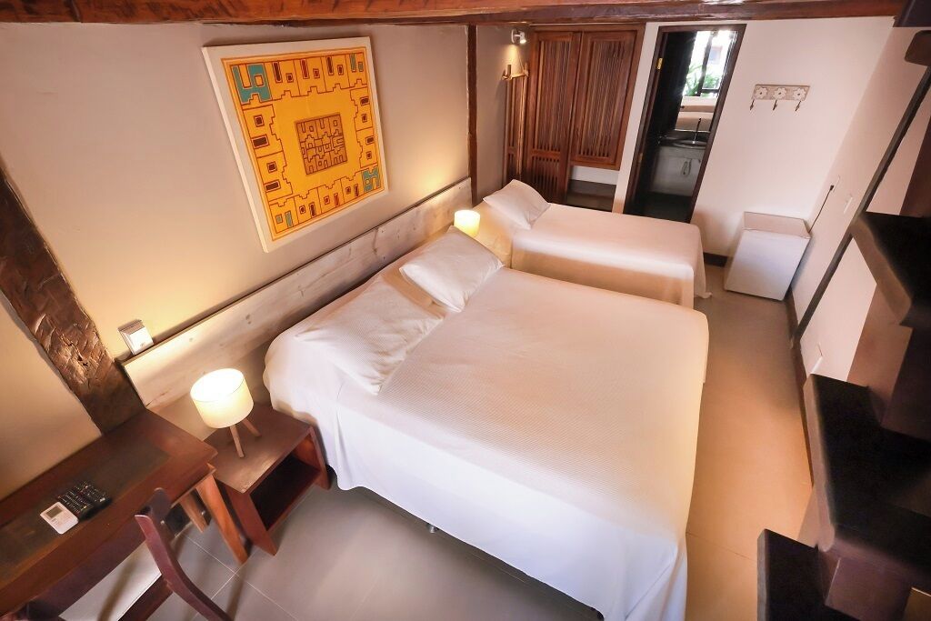 A hotel room with two beds, a desk, a chair, a lamp, and a wall map.