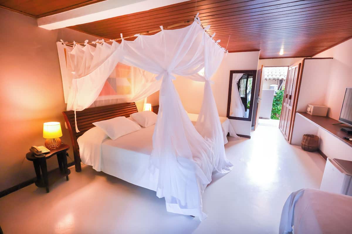 A bedroom with a four-poster bed, bedside tables, a lamp, and a television.