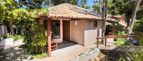 A small, single-story building with a tiled roof, a covered porch, and a small pond.