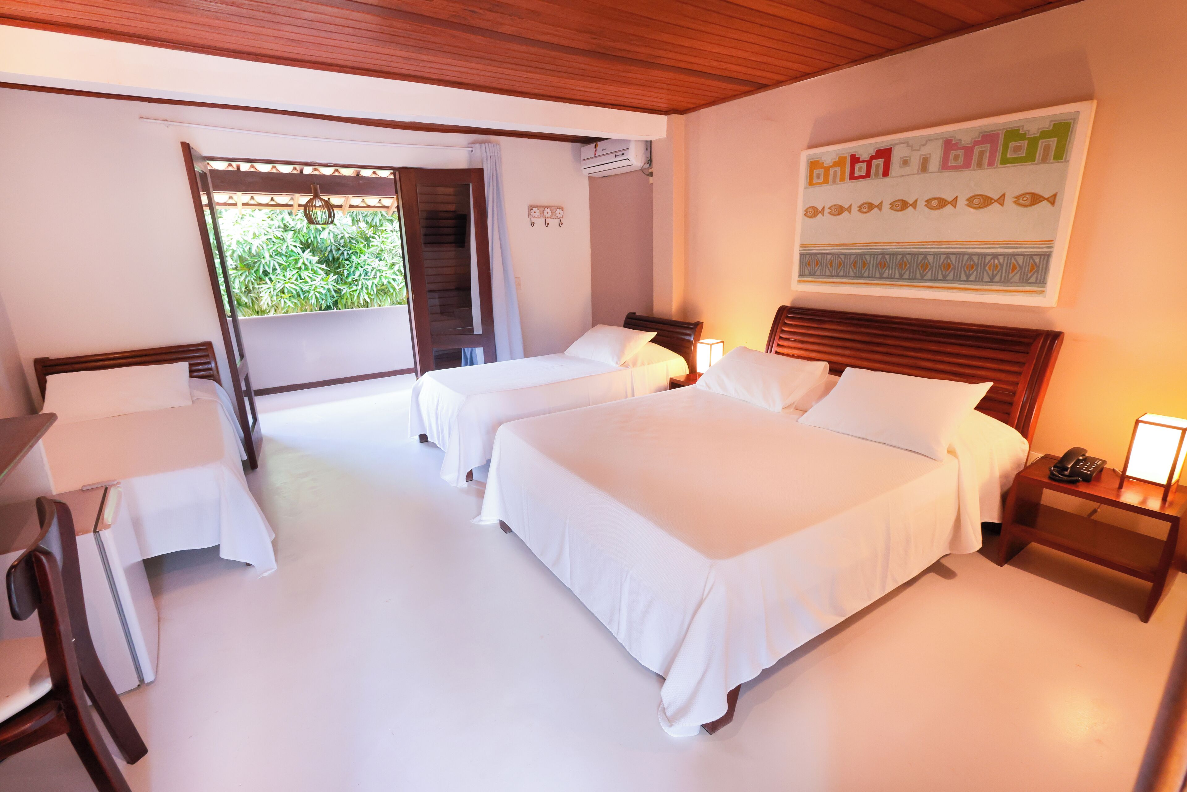 A hotel room with two beds, a desk, and a chair. There is a window with a view of greenery outside.