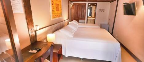 A hotel room with a bed, a desk with a lamp, a TV, and a poster on the wall.