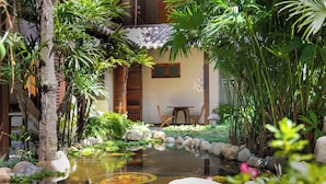 Un jardín tranquilo con un estanque, una mesa de madera y un edificio con tejado de azulejos.