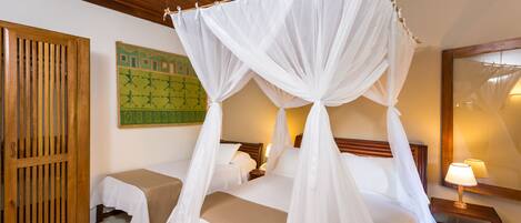 Een hotelkamer met een hemelbed, een houten deur, een klein tafeltje met een lamp en een groene wanddecoratie.