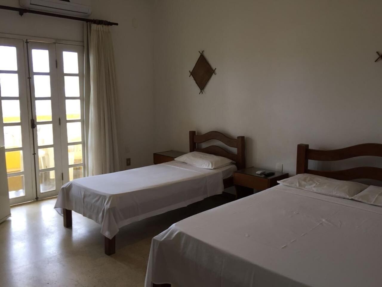 A room with two beds, a nightstand, a wall-mounted clock, and a sliding glass door leading to an outdoor area.