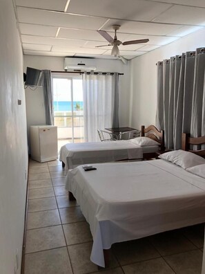 Habitación de hotel con dos camas, una mesita, un televisor, un ventilador de techo y vista al océano.