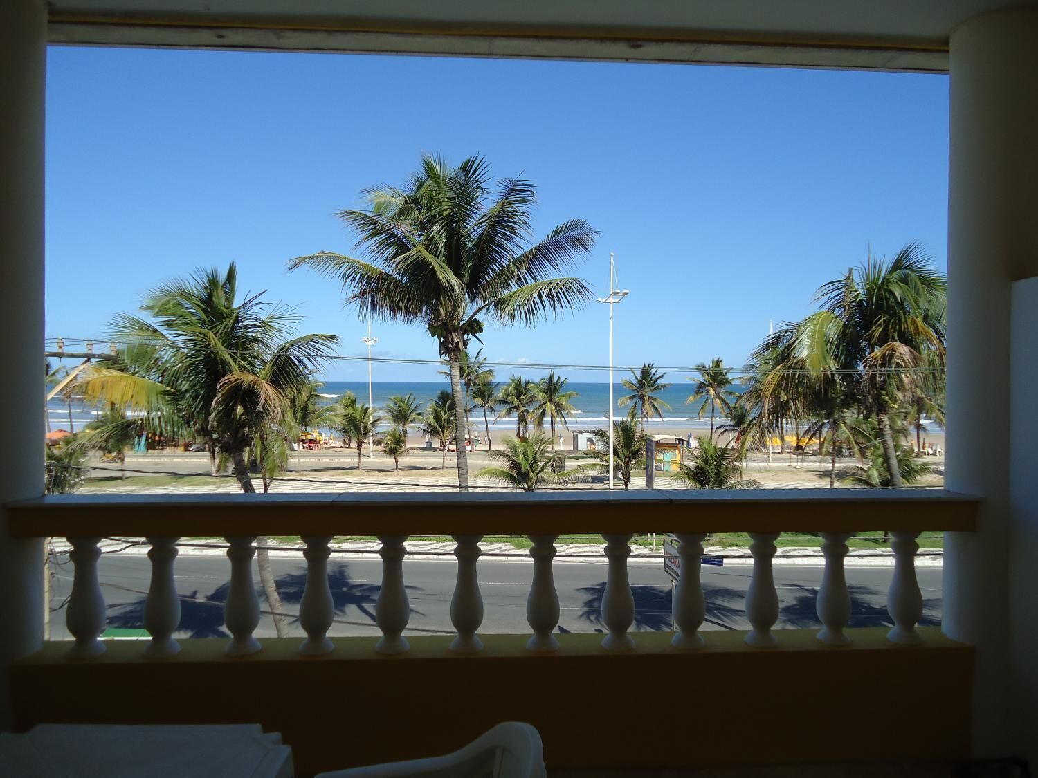 Un balcone con vista sulla spiaggia, palme e cielo sereno.