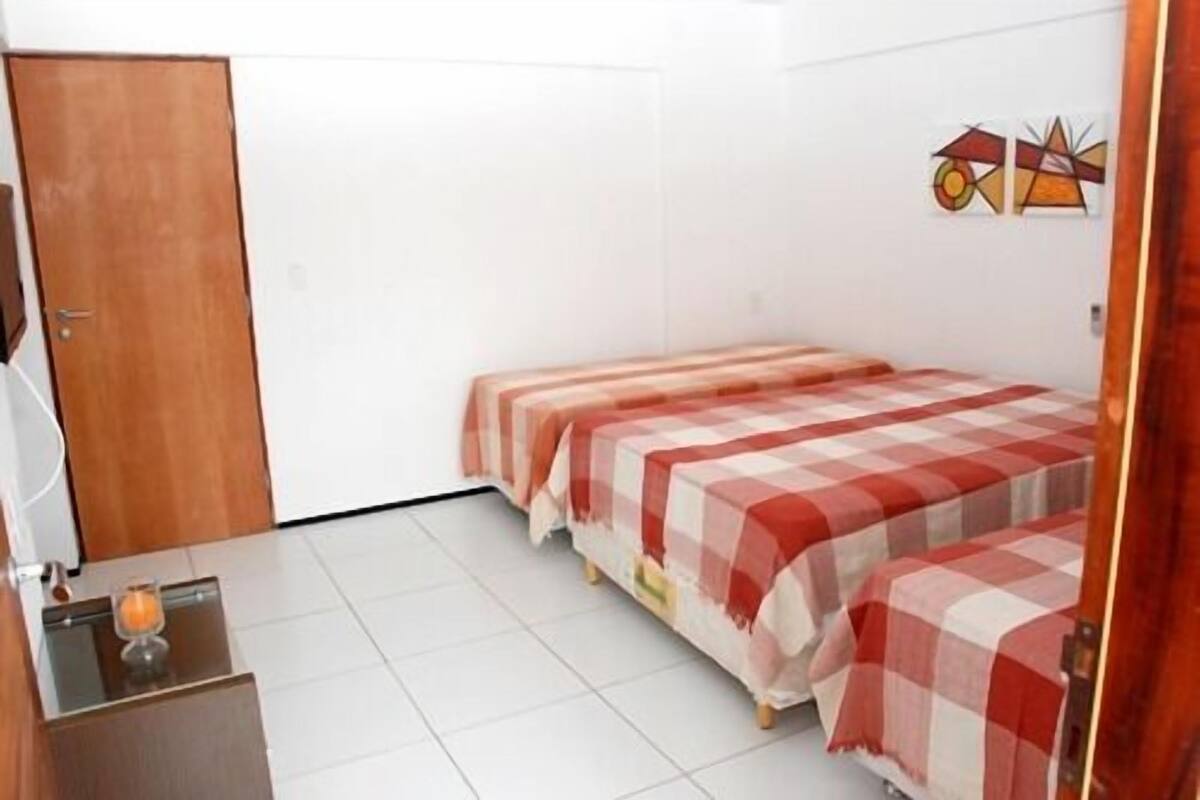 Une petite pièce propre, avec deux lits, une porte en bois et une petite table sur laquelle se trouve une bougie.