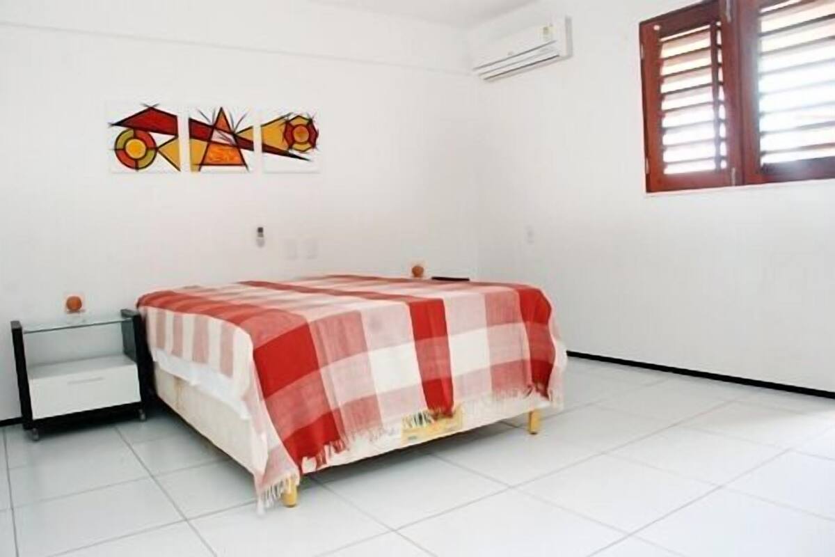 Une chambre à coucher comprenant un lit, une table de chevet, une fenêtre avec des stores et un mur orné d’œuvres d’art abstraites.