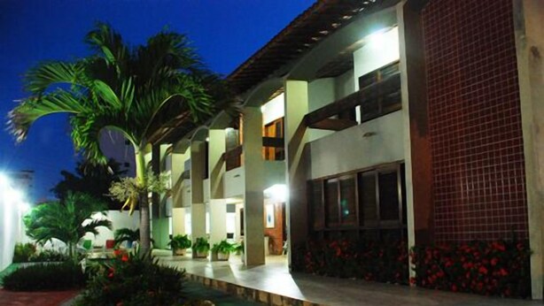 A hotel with a covered outdoor area, palm trees, and a red-tiled wall. - Pousada Costa Marina (Fortaleza)