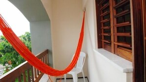 A balcony with a red hammock, a white plastic chair, and wooden window frames. - Pousada Costa Marina (Fortaleza)