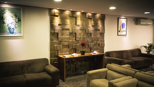 A reception area with a modern design, featuring a patterned wall, a wooden reception desk, and two sofas. - Syros Hotel (Gama)
